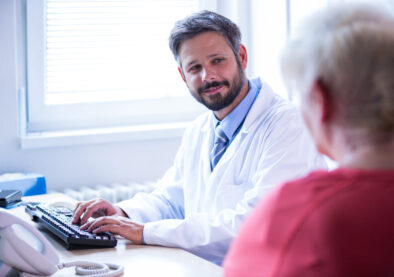 Doctor interacting with patient while working on computer in medical office at hospital